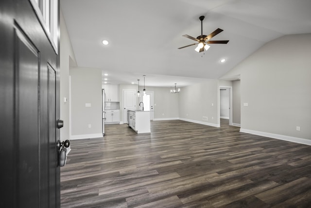 unfurnished living room with lofted ceiling, ceiling fan with notable chandelier, a sink, dark wood finished floors, and baseboards