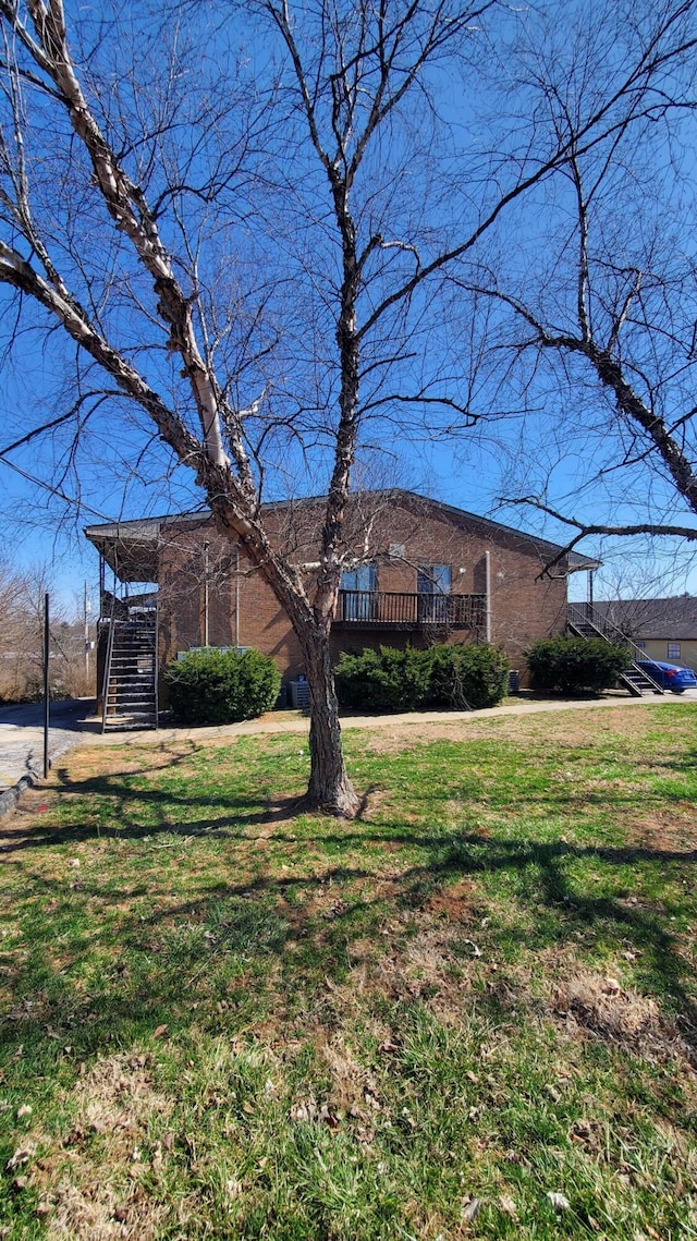 view of front of home featuring brick siding, stairway, a wooden deck, and a front lawn