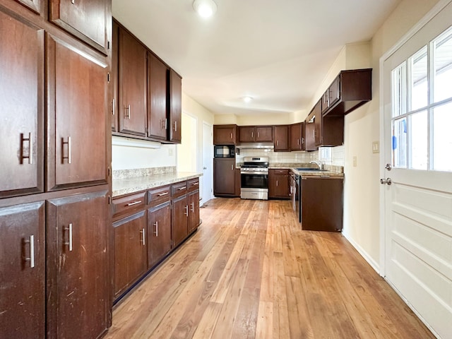 kitchen with stainless steel gas range oven, light wood-style flooring, a sink, black microwave, and decorative backsplash