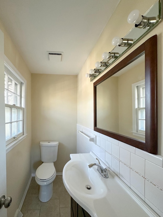 half bathroom featuring tile patterned floors, visible vents, toilet, a sink, and baseboards