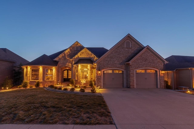 french country inspired facade featuring brick siding, a yard, concrete driveway, and a garage