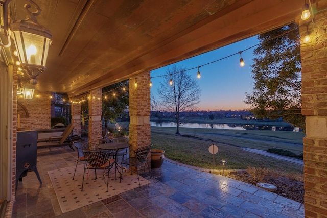 patio terrace at dusk featuring outdoor dining area and a water view