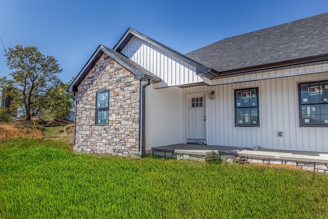 doorway to property with a porch, a shingled roof, a yard, and board and batten siding