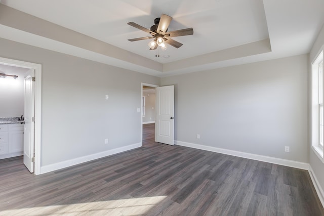 unfurnished bedroom featuring a raised ceiling, dark wood-style floors, baseboards, and ceiling fan