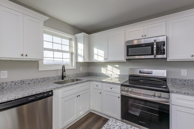 kitchen with dark wood-type flooring, a sink, light stone counters, appliances with stainless steel finishes, and white cabinets