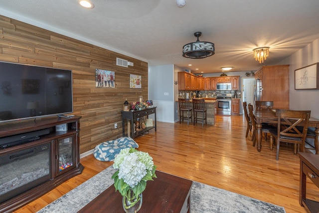 living area featuring recessed lighting, visible vents, light wood-type flooring, and wood walls