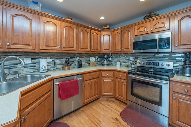 kitchen featuring light wood finished floors, a sink, appliances with stainless steel finishes, brown cabinetry, and light countertops