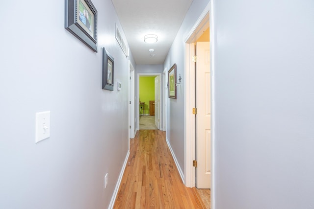 hallway with visible vents, light wood-style floors, and baseboards