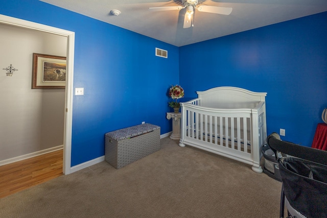 carpeted bedroom featuring visible vents, baseboards, a nursery area, and a ceiling fan