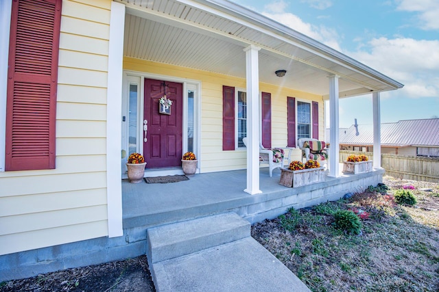 view of exterior entry with a porch and fence