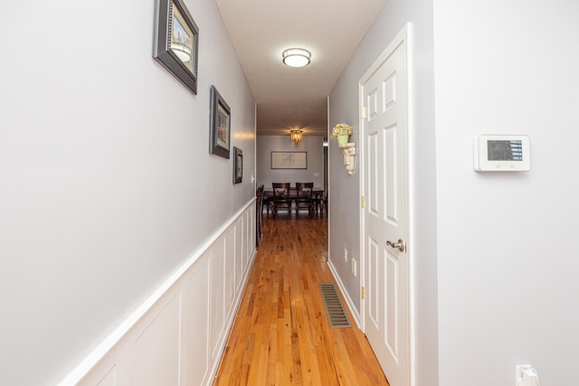 hall with a wainscoted wall, light wood-style flooring, and a decorative wall