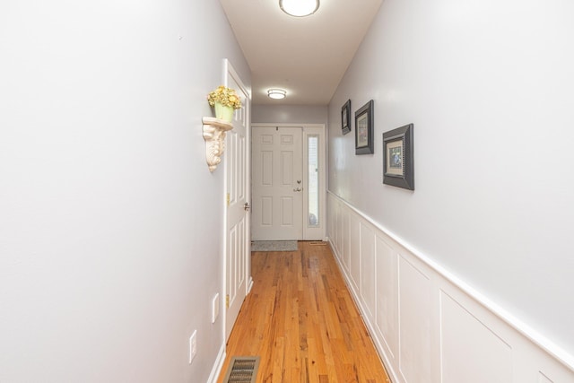 hallway featuring a decorative wall, light wood-style flooring, visible vents, and wainscoting