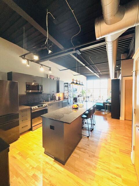 kitchen featuring a sink, a center island, light wood-style floors, appliances with stainless steel finishes, and decorative backsplash