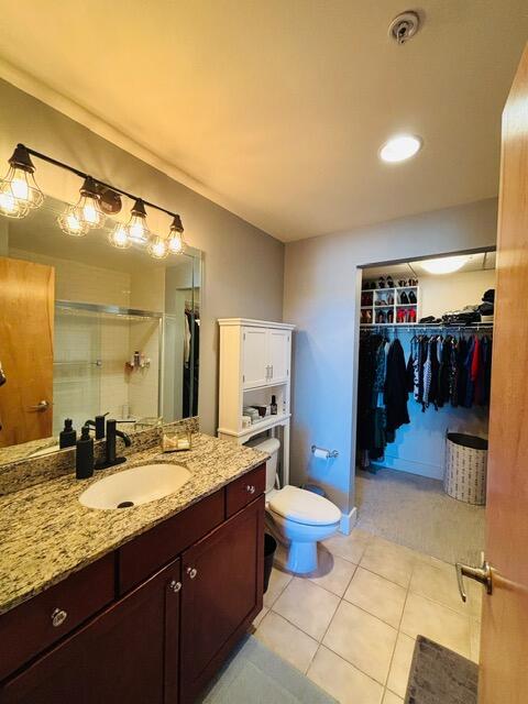 full bath featuring a walk in closet, toilet, a stall shower, tile patterned floors, and vanity