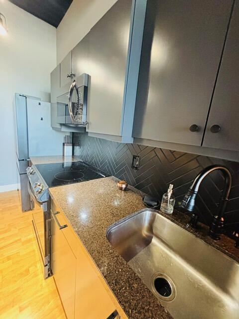 kitchen featuring dark stone countertops, a sink, appliances with stainless steel finishes, light wood-type flooring, and backsplash