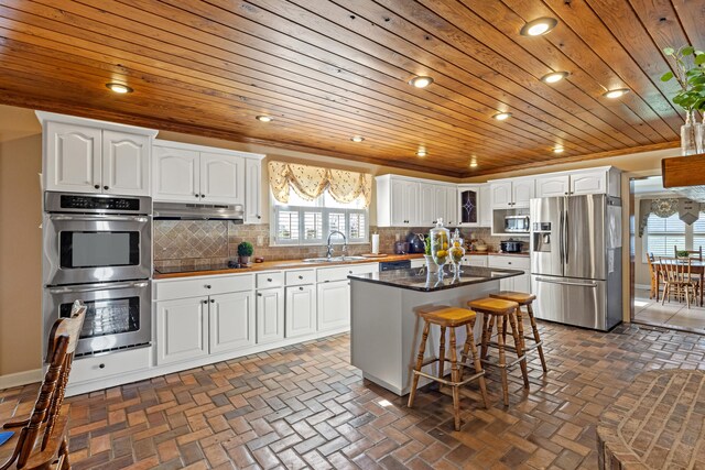 kitchen with tasteful backsplash, appliances with stainless steel finishes, wooden ceiling, and brick floor