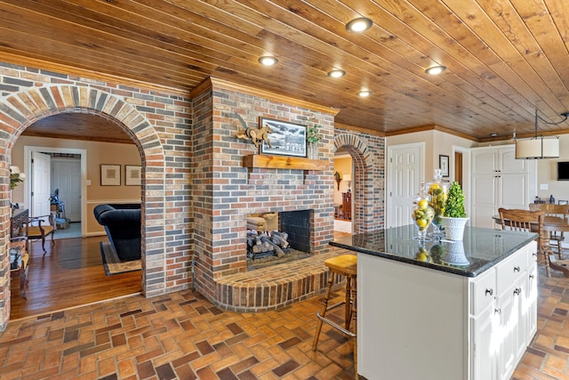 kitchen with a brick fireplace, crown molding, wooden ceiling, brick floor, and arched walkways