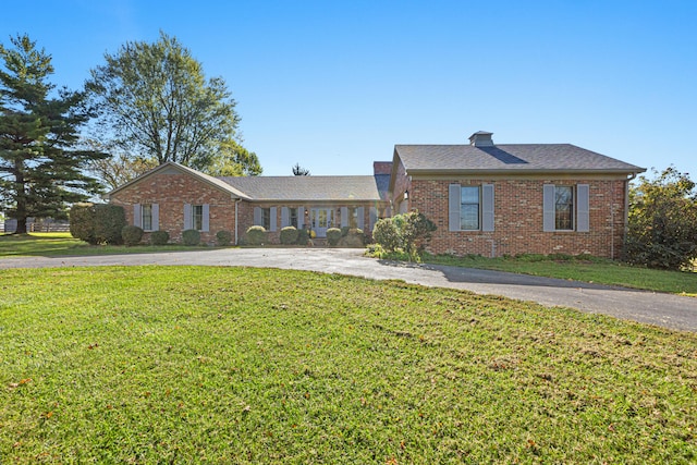 view of front of house with aphalt driveway, brick siding, a front lawn, and a chimney