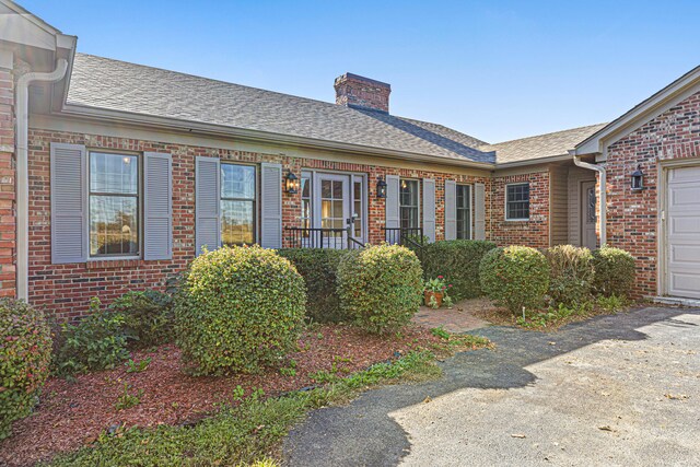 exterior space featuring an attached garage, brick siding, roof with shingles, and a chimney