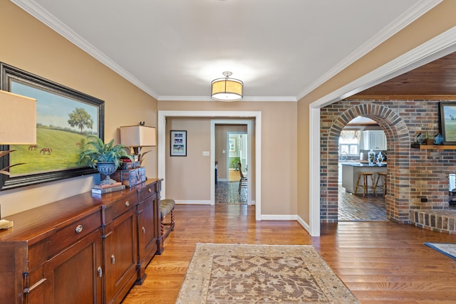 entryway with baseboards, arched walkways, light wood-style floors, and ornamental molding