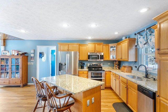 kitchen with light stone countertops, light wood-style flooring, a sink, appliances with stainless steel finishes, and a center island