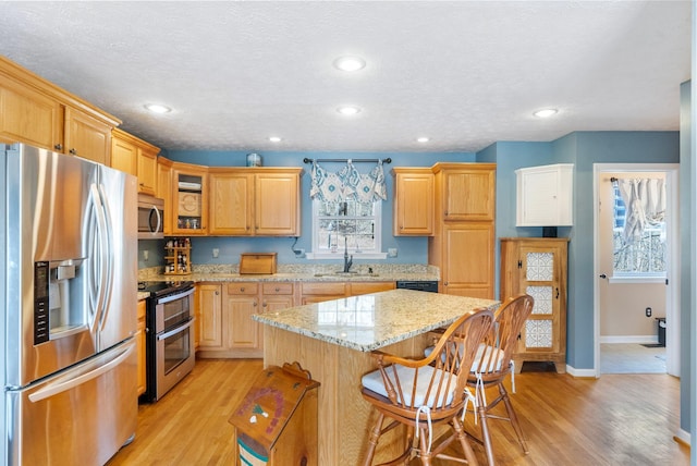 kitchen featuring light wood-style flooring, glass insert cabinets, appliances with stainless steel finishes, and a sink