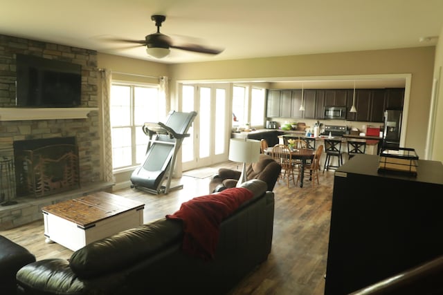 living room featuring a stone fireplace, wood finished floors, and ceiling fan