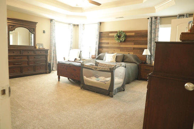 bedroom featuring ceiling fan, a tray ceiling, light carpet, and ornamental molding