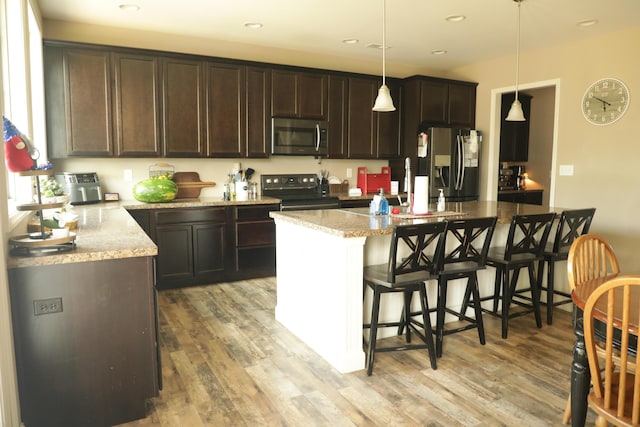 kitchen featuring light wood-style floors, dark brown cabinetry, appliances with stainless steel finishes, and a breakfast bar area