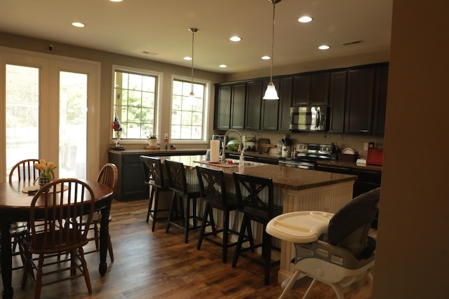 kitchen with a center island with sink, visible vents, dark wood-type flooring, appliances with stainless steel finishes, and a kitchen bar