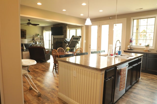 kitchen with a brick fireplace, open floor plan, dishwasher, wood finished floors, and a sink