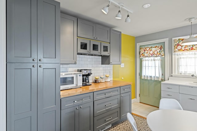 kitchen with light tile patterned floors, decorative backsplash, white microwave, and gray cabinets