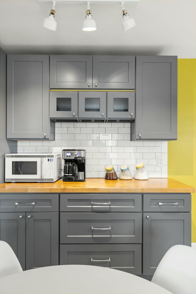 kitchen featuring white microwave, gray cabinets, tasteful backsplash, and wood counters