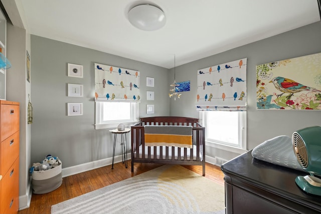 bedroom featuring a crib, baseboards, and wood finished floors