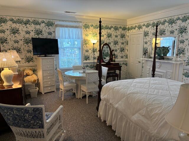 carpeted bedroom featuring visible vents, wainscoting, wallpapered walls, and crown molding