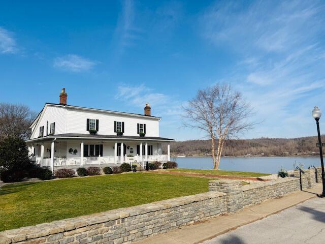 view of front facade with covered porch, a chimney, a front lawn, and a water view