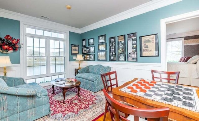 living area featuring visible vents, crown molding, and a wainscoted wall