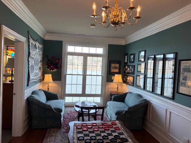 living area with a notable chandelier, a decorative wall, a wainscoted wall, and ornamental molding