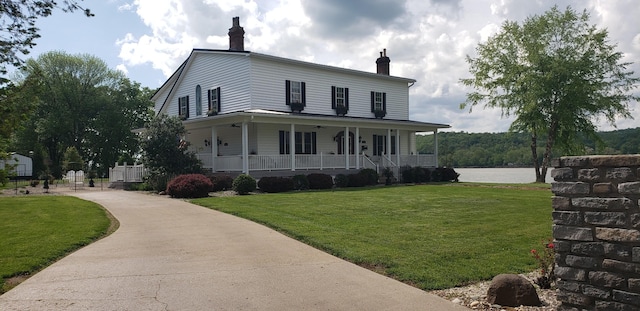 farmhouse featuring a front lawn, a porch, concrete driveway, and a chimney