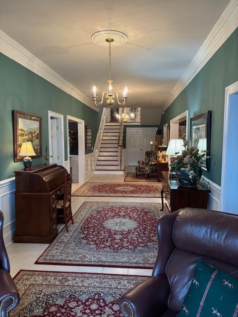 tiled living area with a wainscoted wall, an inviting chandelier, ornamental molding, and stairs