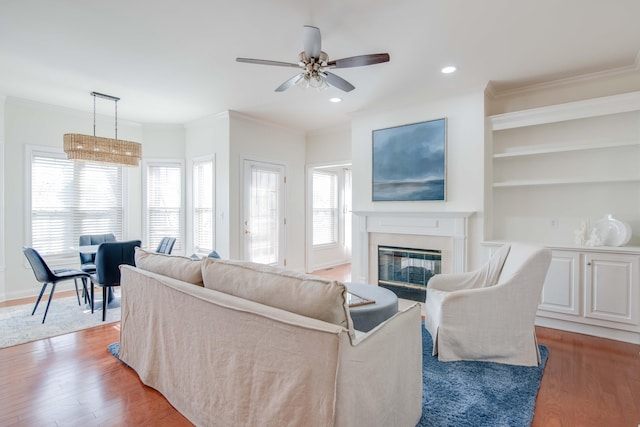 living area with light wood finished floors, crown molding, baseboards, recessed lighting, and a glass covered fireplace