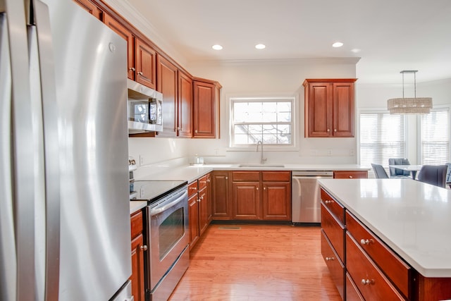 kitchen featuring ornamental molding, a sink, light wood-style floors, appliances with stainless steel finishes, and light countertops