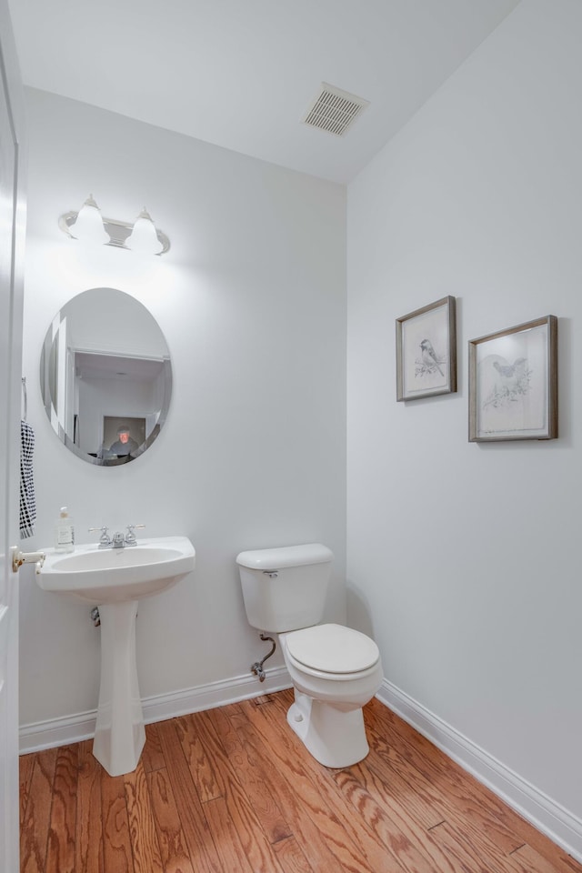 half bath with visible vents, baseboards, toilet, and wood finished floors