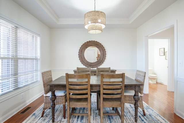 dining space with a raised ceiling, a healthy amount of sunlight, and wood finished floors