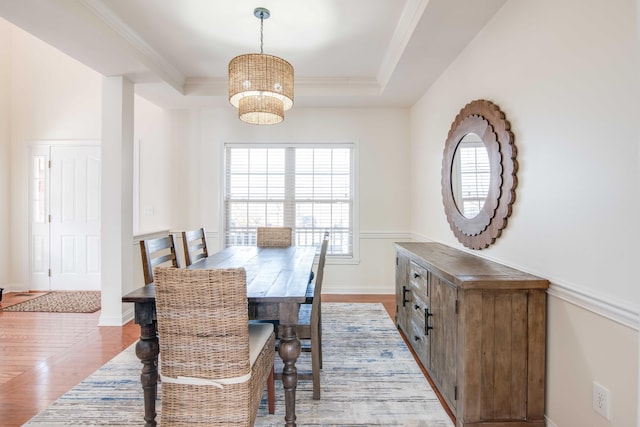 dining space with a raised ceiling, a notable chandelier, crown molding, and light wood finished floors