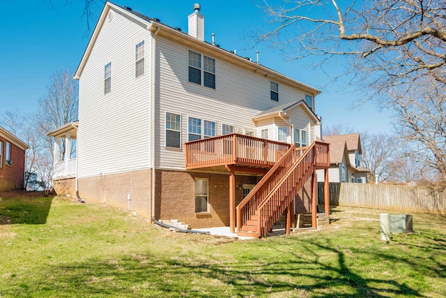 rear view of property featuring brick siding, a deck, a yard, and fence