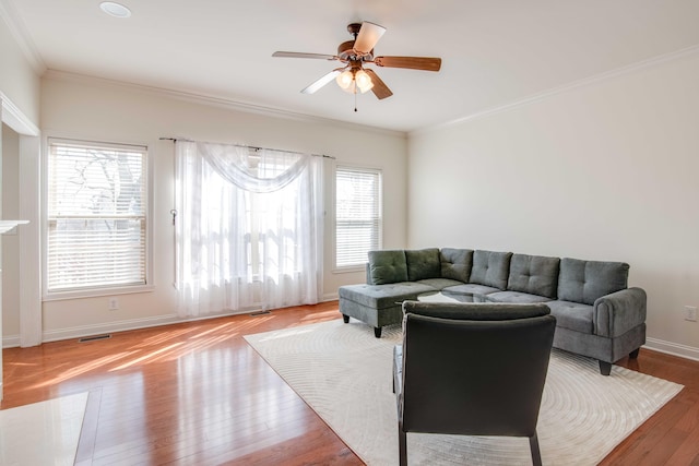 living area with visible vents, a ceiling fan, wood finished floors, crown molding, and baseboards