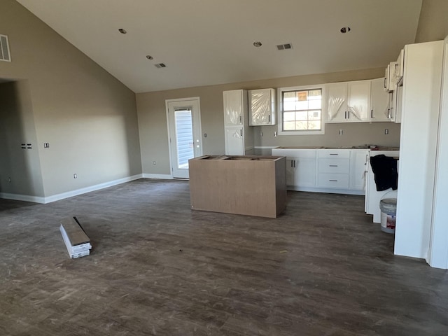 kitchen with visible vents, a kitchen island, baseboards, open floor plan, and white cabinets