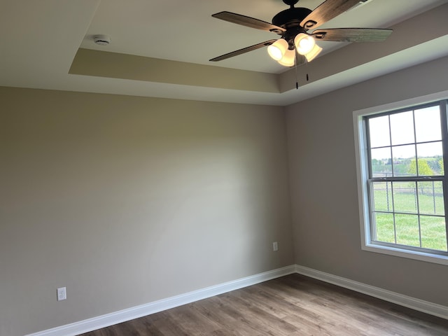 empty room featuring wood finished floors, a ceiling fan, baseboards, and a healthy amount of sunlight