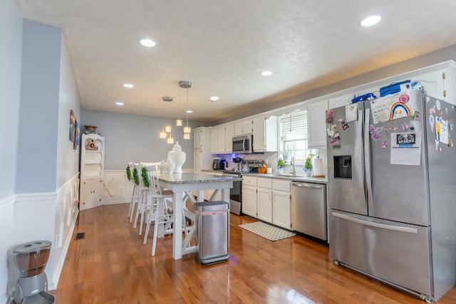 kitchen featuring a kitchen island, a wainscoted wall, stainless steel appliances, hardwood / wood-style flooring, and white cabinetry